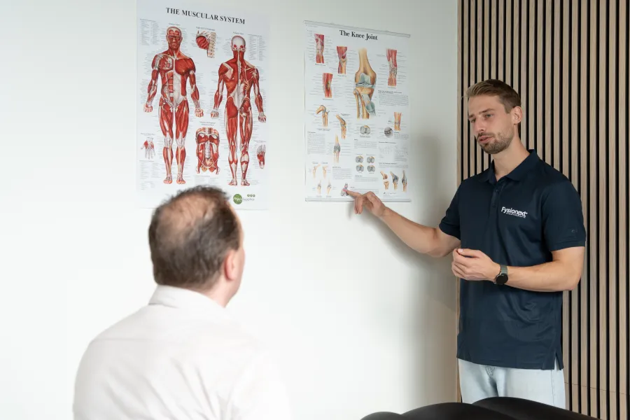 Fysiotherapeut wijst op een anatomiekaart en bespreekt de klacht met een patiënt